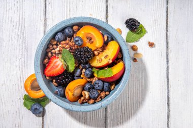Meyve ve böğürtlenli granola kahvaltısı, yaz tatili lezzetli kahvaltı kasesi bol meyve ve böğürtlenli, süt testisi beyaz ahşap masada.