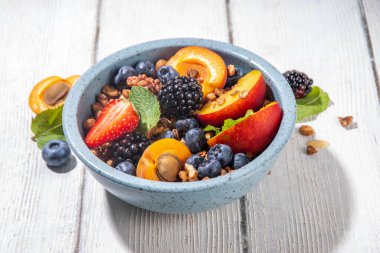 Meyve ve böğürtlenli granola kahvaltısı, yaz tatili lezzetli kahvaltı kasesi bol meyve ve böğürtlenli, süt testisi beyaz ahşap masada.