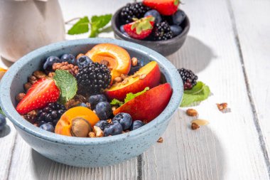 Meyve ve böğürtlenli granola kahvaltısı, yaz tatili lezzetli kahvaltı kasesi bol meyve ve böğürtlenli, süt testisi beyaz ahşap masada.