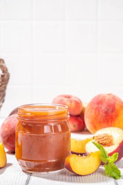 Ev yapımı şeftalili, şeftalili reçel baharat ve kuru üzümlü, küçük kavanozda, taze olgun şeftalili, beyaz ahşap masada.
