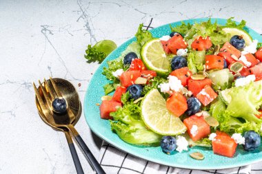 Summer watermelon salad. Fresh raw green salad with lettuce, arugula, watermelon slices, blueberry, feta cheese and honey