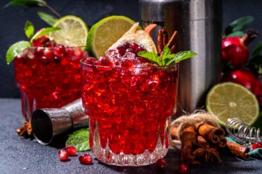 Spicy autumn pomegranate cocktail. Alcohol warming gin drink with pomegranate, lime, cinnamon, mint, autumn winter sangria on dark background copy space