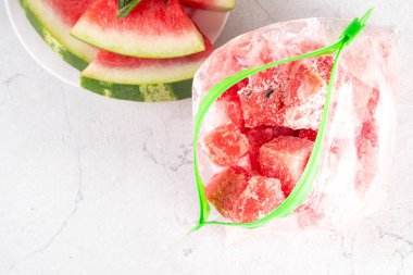 Donmuş karpuz dilimleri, donmuş poşetlerdeki taze çiğ karpuzlar mutfak masasındaki beyaz masa, sağlıklı basit konserve, kış konsepti için dondurulmuş meyve hasadı stokları.. 