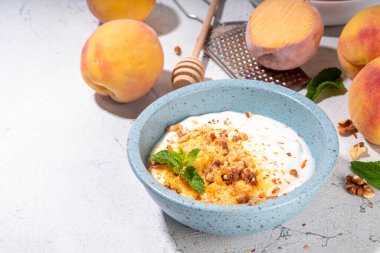 Dondurulmuş şeftali ve krema, kremalı ve yoğurtlu sağlıklı yaz atıştırması ve dondurulmuş şeftali meyveleri, fındık, bal ve nane, kopyalama alanı.