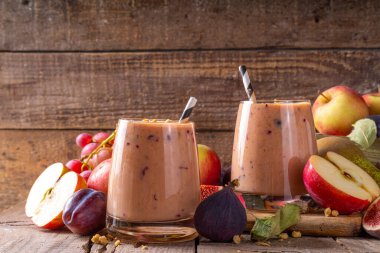 Sonbahar meyveli yoğurt içeceği. Taze meyve, erik, incir, elma, yulaf ve fındık, ahşap arka plan fotokopi alanı ile iki bardak çırpılmış meyve suyu.