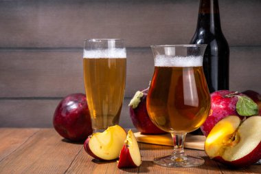 Ekşi elma suyu, elma suyu, elma şarabı veya bira ile dolu bardaklar taze kırmızı elma dilimleri ile ahşap masada.