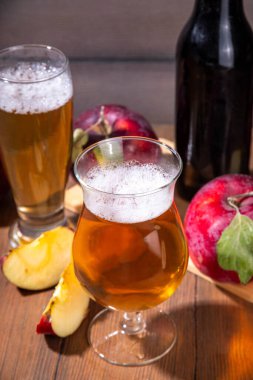 Ekşi elma suyu, elma suyu, elma şarabı veya bira ile dolu bardaklar taze kırmızı elma dilimleri ile ahşap masada.