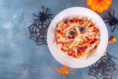 Cadılar Bayramı yemeği ya da akşam yemeği için komik çocuk yemekleri. Sosisli spagetti makarna ketçaplı mumyaların yaratıcı tarifi. Mavi beton masa üzerinde Cadılar Bayramı dekorasyonu.