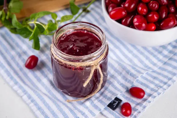 stock image Cornelian cherry, dogwoods edible berry jam or marmalade in small jar with fresh berries on kitchen table, copy space