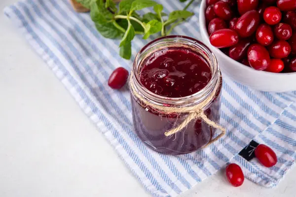 stock image Cornelian cherry, dogwoods edible berry jam or marmalade in small jar with fresh berries on kitchen table, copy space