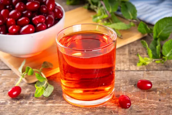 stock image Cornelian cherry, dogwoods edible berry  juice or liquor in glass, on wooden table background, with mint and fresh cornus berry copy space