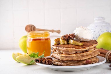 Sweet autumn apple pie pancakes stack with ice cream and caramelized apples on top, won kitchen table with spices, apples and honey jar, copy space clipart