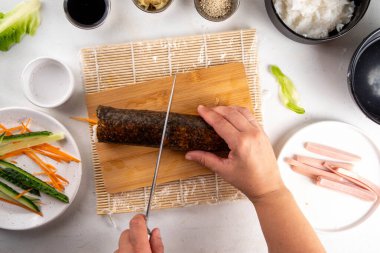 Geleneksel Kore kimbap 'ı, jambon, sebze ve marullu. Yemek pişirme, ev yapımı kimbap pişirme, aşama aşama pişirme ve kesme ellerini resimde kesme, üst görünüm
