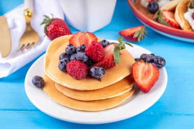 Yaz meyveli geleneksel Amerikan krepleri yığını. Sabah güneşinde bal, çilek ve yabanmersinli kahvaltı krepleri, mavi ahşap arka plan fotokopi alanı.