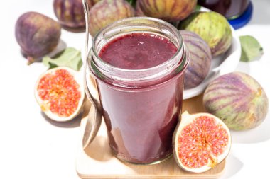 Red fig jam in small jar. Homemade autumn fig jam with fresh fruits. Fall preparations and canning on white table background copy space