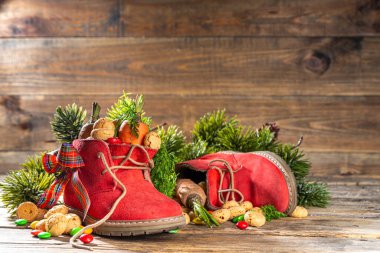 Sinterklaas, Saint Nicholas day background. Little kid red shoe with carrots and sweets, trooigoed, pepernoten, candy. Dutch Christmas holiday on cozy wooden background. 