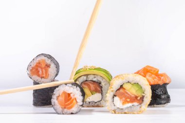 Yaratıcı Japon deniz ürünleri suşisi, suşi ruloları, maki, yemek çubuğu ve beyaz masa üzerinde silah içeren arka plan.