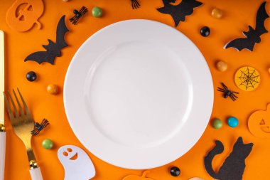 Cadılar Bayramı çocuklarının masa takımları tabak, çatal bıçak takımı ve bayram sembolleri ve renkli arka plan süslemeleri ile üst görünüm fotokopi alanı. Cadılar Bayramı menüsü, davet arkaplanı