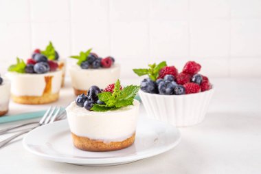 Mini vanilyalı New York peynirli kekleri, kek tavasında pişirilmiş geleneksel cheesecakeler, beyaz mutfak masasında taze böğürtlenler.