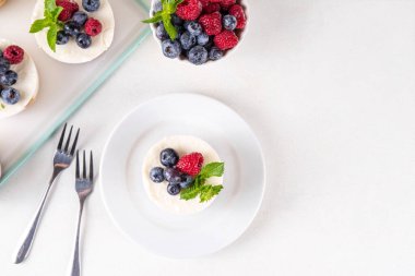 Mini vanilyalı New York peynirli kekleri, kek tavasında pişirilmiş geleneksel cheesecakeler, beyaz mutfak masasında taze böğürtlenler.