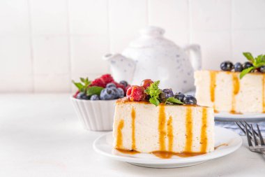 Geleneksel New York peynirli kek dilimleri tabakta, taze böğürtlenler beyaz mutfak masasında