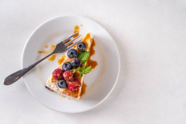 Geleneksel New York peynirli kek dilimleri tabakta, taze böğürtlenler beyaz mutfak masasında