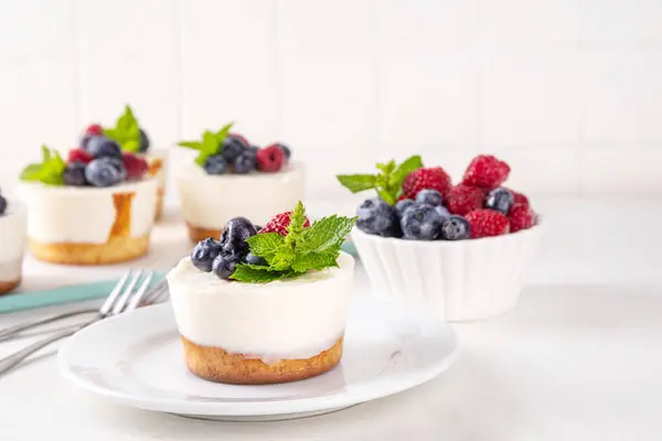 stock image Mini vanilla New York cheesecakes, portioned traditional cheesecakes cooked in muffin pan, with fresh berries on white kitchen table