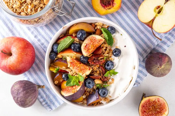 Sağlıklı sonbahar kahvaltı kasesi. Süzme peynir veya yoğurtlu granola, fındık ve sonbahar meyveleri, sabah ve öğle yemekleri için dengeli atıştırmalık, fotokopi alanı. 