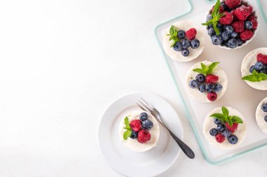 Mini vanilyalı New York peynirli kekleri, kek tavasında pişirilmiş geleneksel cheesecakeler, beyaz mutfak masasında taze böğürtlenler.