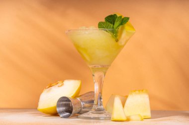 Kavunlu, limonlu ve naneli yaz likörü. Donmuş kavun martinisi ya da bardaklı kokteyl, bej renkli, güneşli arka planda.