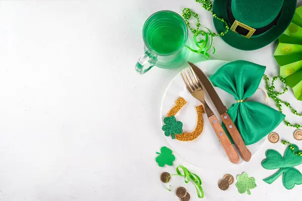 stock image Saint patrick table setting flat lay with cutlery, plate, knife and fork, Patrick day party decor, coins, leprechaun's hat, eyeglasses, lucky horseshoe, confetti, beads on green background