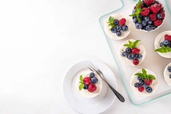 stock image Mini vanilla New York cheesecakes, portioned traditional cheesecakes cooked in muffin pan, with fresh berries on white kitchen table