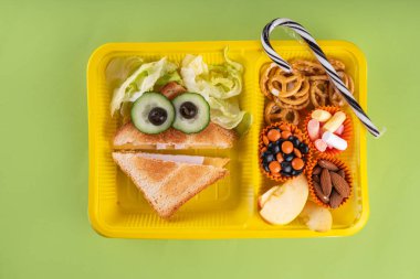 Cadılar Bayramı komik çocuklar, krakerli okul yemeği, sağlıklı peynirli sandviç, kurabiye ve ikramlar, parlak renkli arka plan fotokopi alanı üst görünümü.