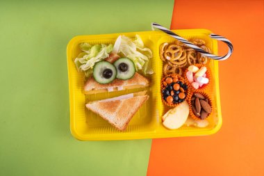 Cadılar Bayramı komik çocuklar, krakerli okul yemeği, sağlıklı peynirli sandviç, kurabiye ve ikramlar, parlak renkli arka plan fotokopi alanı üst görünümü.