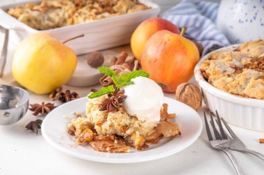  Apple Crumble Dessert, crisp cobbler with Ice Cream, crumble pie with crunchy dough topping in baking dish and plate, with ice cream scoop on white kitchen table clipart