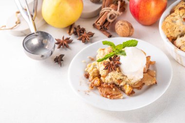  Elmalı gevrek tatlı, dondurmalı çıtır tart, kıtır kıtır hamurlu turta fırın tabağında ve tabakta, dondurma kepçesiyle beyaz mutfak masasında.