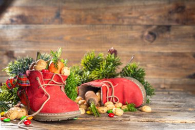 Sinterklaas, Saint Nicholas day background. Little kid red shoe with carrots and sweets, trooigoed, pepernoten, candy. Dutch Christmas holiday on cozy wooden background. 