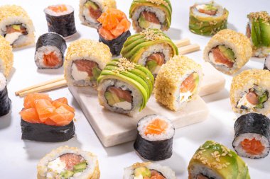 Yaratıcı Japon deniz ürünleri suşisi, suşi ruloları, maki, yemek çubuğu ve beyaz masa üzerinde silah içeren arka plan.