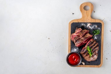 Ahşap kesme tahtasında ızgara biftek, ketçap sosu ve baharat, üst görünüm kopya alanı.