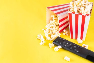 Renkli parlak arka planda televizyon kumandalı kağıt kaseler dolusu patlamış mısır. Televizyon, film galası, TV dizisi, spor, dizi izlemenin tadını çıkarın. Düz yatış, üst görünüm 