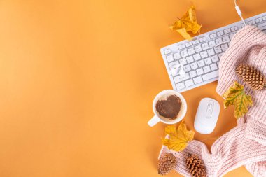 Sonbahar tatillerinde rahat bir arka plan, kahve fincanı ve kalp dekoru, bilgisayar klavyesi, kulaklık, sıcak süveter ya da ekose, bej arka planda düşme yaprakları. 