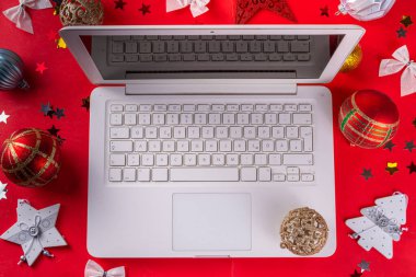 Yılbaşı arkaplanında beyaz dizüstü bilgisayar klavyesi ve kış tatili dekorasyonu parlak kırmızı arka planda süsleri var. Noel alışverişi, tatil hazırlıkları, üst görünüm kopya alanı