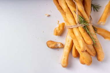 İtalyan Akdeniz Grissini ekmek çubukları, beyaz mutfak arka planında aromatik yağ ve biberiye filizleri ile