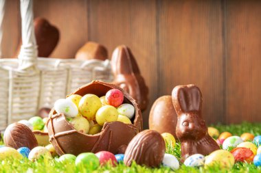 Easter egg hunting background. Various candy and chocolate Easter eggs, bunny and rabbits with basket for eggs on green grass park or garden background