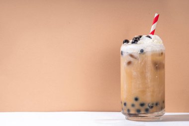 Klasik boba köpüklü çay tapyoka incileri ve sütsüz krema bardağın üstünde, yaz soğuk tatlı içeceği beyaz masa arkasında fotokopi alanı