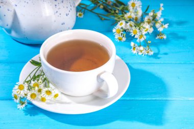 Bitkisel organik papatya çayı ve taze vahşi yaz papatya çiçekleri, beyaz fincanda, çaydanlık kopyasıyla birlikte.