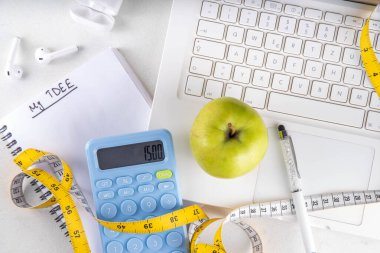 Kalori hesap makinesi, sağlıklı TDEE konsepti. Toplam günlük enerji harcamalarına dayanan kalori hesaplaması, hesap makinesi, defter, mezura, elma. Sağlıklı kilo verme diyeti arka planı