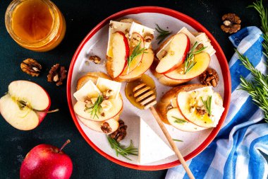 Sonbahar Elmalı Brie Crostini, Ceviz ve Bal, Sonbahar yemeği, Şükran Günü parti aperatifleri. Kırmızı elma dilimli küçük sandviçler, brie peyniri ve tatlı bal çiselemeleri.