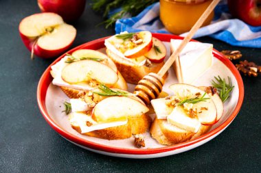 Sonbahar Elmalı Brie Crostini, Ceviz ve Bal, Sonbahar yemeği, Şükran Günü parti aperatifleri. Kırmızı elma dilimli küçük sandviçler, brie peyniri ve tatlı bal çiselemeleri.