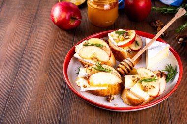 Sonbahar Elmalı Brie Crostini, Ceviz ve Bal, Sonbahar yemeği, Şükran Günü parti aperatifleri. Kırmızı elma dilimli küçük sandviçler, brie peyniri ve tatlı bal çiselemeleri.